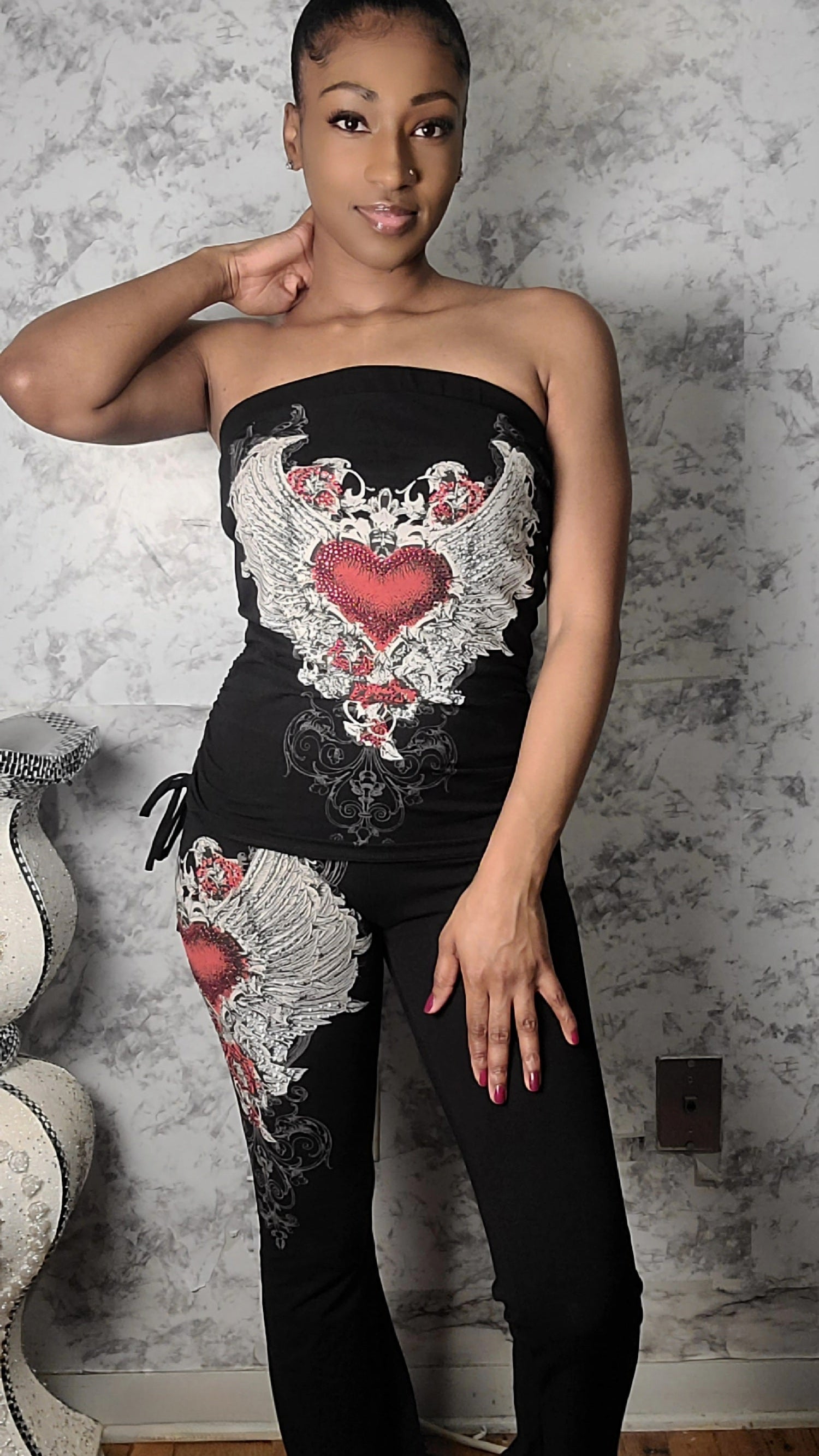Woman wearing a black strapless top with floral designs against a textured wall.