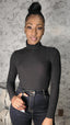 Woman wearing a black turtleneck and jeans against a textured wall.