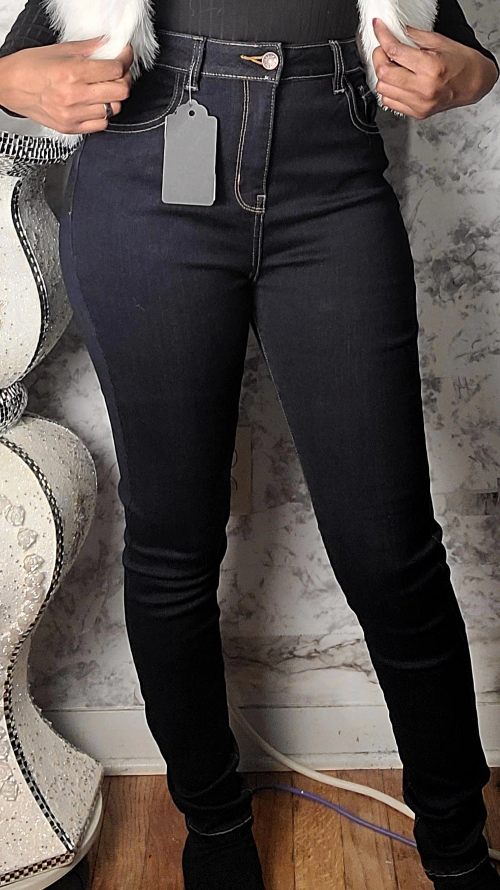 Person wearing black jeans with a visible tag, standing against a marble wall.