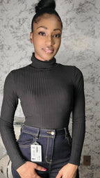 Woman wearing a black ribbed turtleneck and dark jeans with a visible tag.