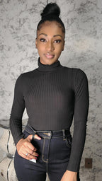 Woman wearing a black turtleneck and jeans against a textured wall.