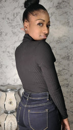 Person wearing a dark gray long-sleeve shirt and blue jeans on a textured wall background