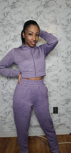 Woman wearing a purple textured outfit against a marble wall.