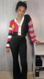 Person wearing a colorful striped cardigan over a crop top and black pants against a gray wall.