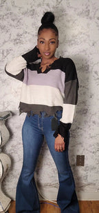 Woman wearing a colorful sweater and blue jeans against a textured wall.
