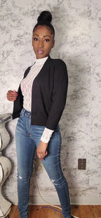 Woman wearing a black blazer, white blouse, and blue jeans against a textured wall.