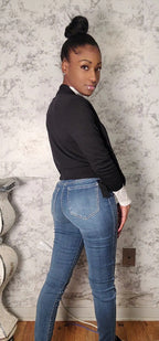 Woman wearing a black top and blue jeans against a textured wall.