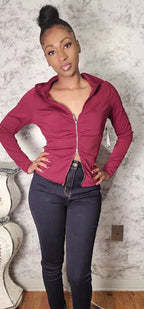 Woman wearing a pink zip-up hoodie and dark jeans against a textured wall.
