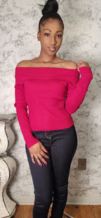 Woman wearing a bright pink off-shoulder sweater and black pants against a textured wall.